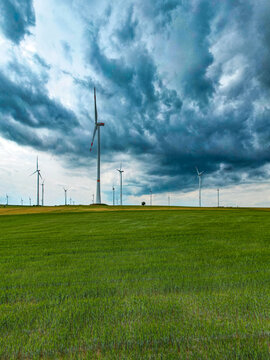 Aerial view of wind turbines standing in a vast green field under a dramatic stormy sky in Worms, Rhineland-Palatinate, Germany.