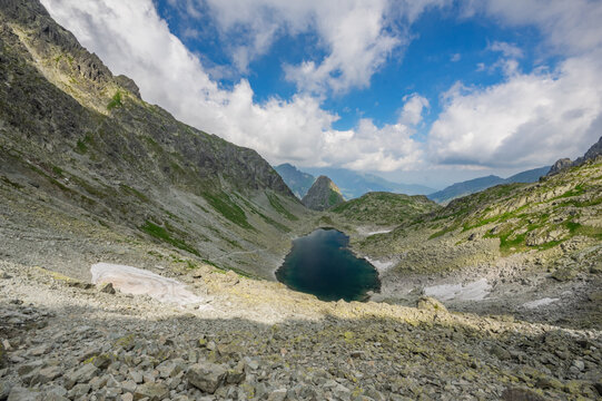 View of Zamrznute pleso surrounded by rocky mountain slopes and patches of snow under a blue sky in Tatranska Javorina, Presovsky kraj, Slovakia.
