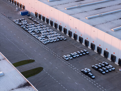 Aerial view of a large logistics warehouse facility with rows of parked cars in the loading bay area in Gdansk, Pomeranian Voivodeship, Poland.