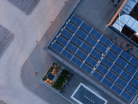 Aerial view of solar panels installed on a flat building roof with a parking lot and green space in Gdansk, Pomeranian Voivodeship, Poland.