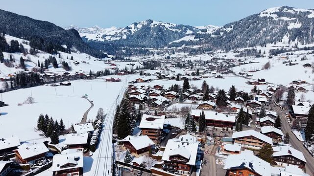 Aerial view of Gstaad village with snow-covered chalets and surrounding alpine mountains in Saanen, Canton of Bern, Switzerland.