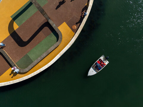 Aerial view of Salinas de Marinha da Noeirinha with a small motorboat on the water and people walking along the colorful paved walkway, Vera Cruz, Aveiro, Portugal.