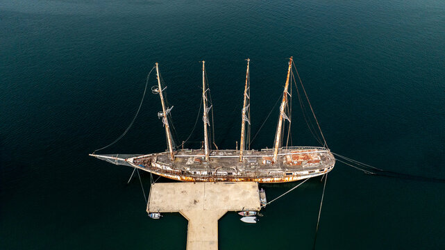 Aerial view of a weathered four-masted sailing ship docked at a concrete pier in the calm waters of the Aveiro lagoon, Vera Cruz, Aveiro, Portugal.