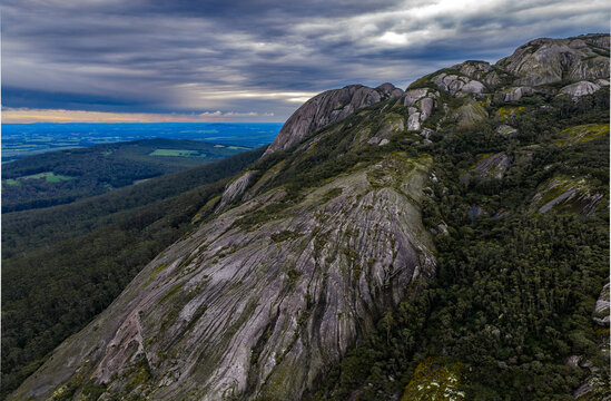 Aerial view of Devil's Slide granite formation surrounded by dense forest under a dramatic cloudy sky in Porongurup, Western Australia, Australia.