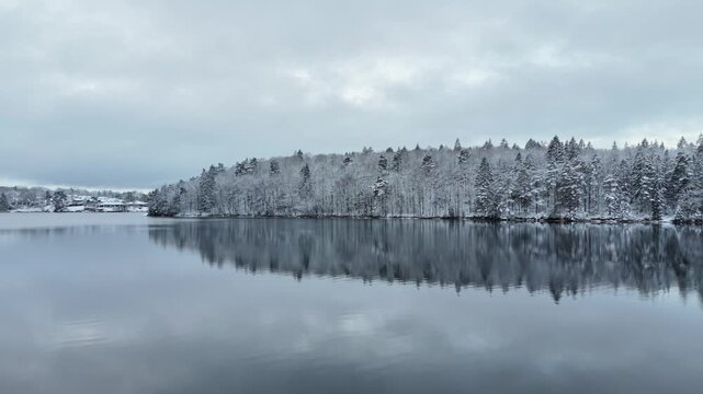 Aerial view of Stora Kasjon lake surrounded by snow-covered pine forest under a cloudy sky in Ojersjo, Vastra Gotaland County, Sweden.