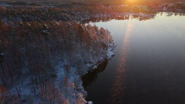 Aerial view of Stora Kasjon surrounded by snow-covered trees during a golden sunset in Ojersjo, Vastra Gotaland Count, Sweden.