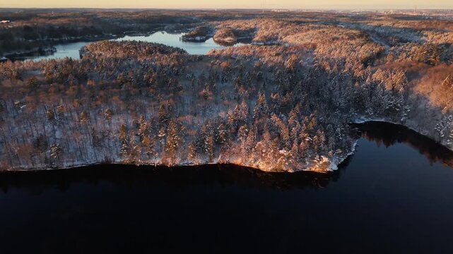 Aerial view of Stora Kasjon surrounded by snow-covered pine forests during golden hour in Ojersjo, Vastra Gotaland Count, Sweden.