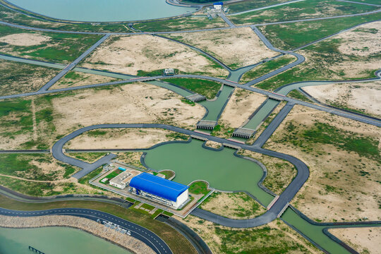 Aerial view of Tekong Island featuring a modern blue-roofed facility, interconnected water channels, and paved roads surrounded by reclaimed land Singapore, Singapore.
