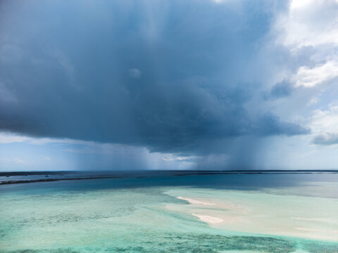 Aerial view of turquoise waters and sandbars under a dramatic dark storm cloud with rain falling over the ocean in Rolleville, Exuma, The Bahamas.