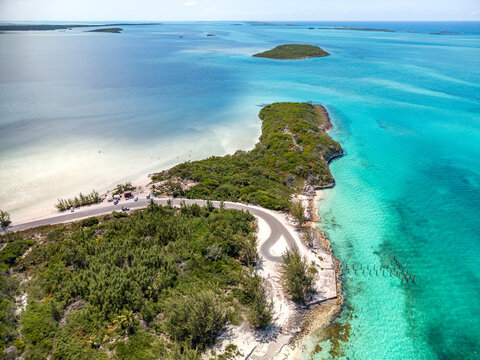 Aerial view of the coastline at Rolleville, featuring a winding road along the lush green peninsula, turquoise waters, and sandy beaches in Rolleville, Exuma, The Bahamas.