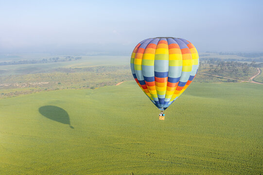 Aerial view of a colorful hot air balloon floating above the green fields of Kibbutz Ruhama, South District, Israel.