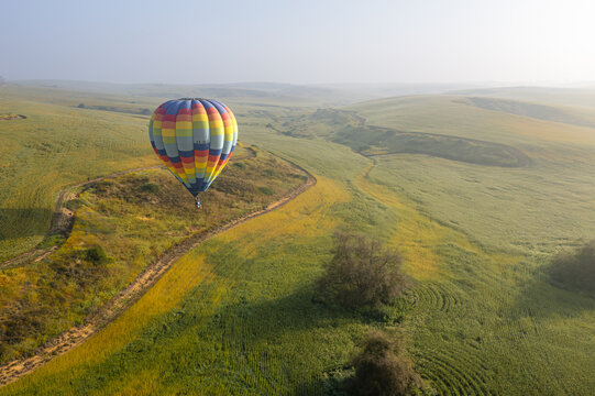 Aerial view of a colorful hot air balloon floating over the rolling green hills and fields of Kibbutz Ruhama, South District, Israel.