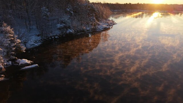 Aerial view of Stora Kasjon with snow-covered trees and mist rising from the water during a golden sunrise in Ojersjo, Vastra Gotaland County, Sweden.