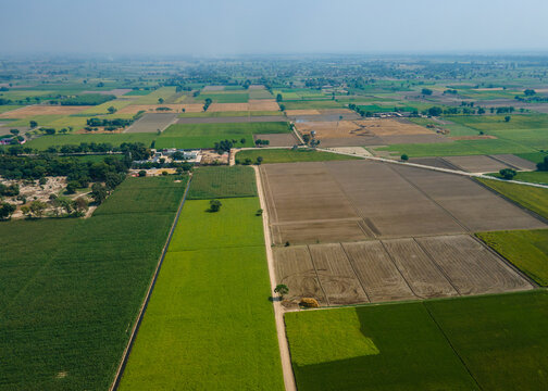 Aerial view of agricultural land with various crop fields, dirt paths, and rural landscape, Punjab, Pakistan.