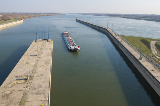 Aerial view of a cargo ship navigating through the Gabcikovo Dam locks on the Danube River with concrete walls and calm water in Gabcikovo, Trnavsky kraj, Slovakia.