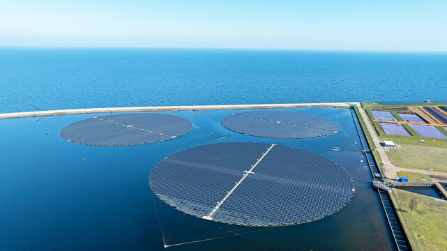 Aerial view of circular floating solar panels installed on a calm lake with a dike and surrounding land in Andijk, North Holland, Netherlands.