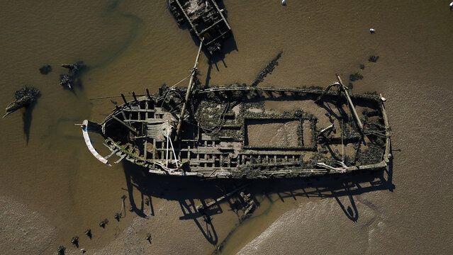 Aerial view of abandoned wooden shipwrecks in the boat cemetery at low tide with mudflats and exposed timber structures in Lanester, Brittany, France.