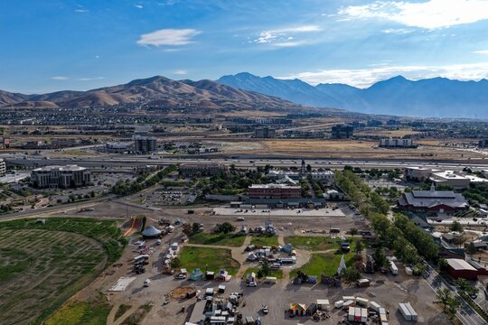 Aerial view of a summer carnival being set up in an open field with Silicon Slopes buildings and Traverse Mountain in the background in Lehi, Utah, United States.
