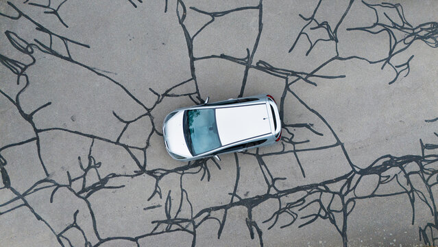 Aerial view of a silver car parked on an asphalt road with visible tar-filled cracks forming a web-like pattern in Trier-Saarburg, Rhineland-Palatinate, Germany.