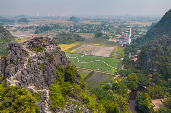 Aerial view of Mua Cave with its stone staircase winding up the limestone karst peak, surrounded by lush greenery and rural landscape in Nam Hoa Lu, Ninh Binh, Vietnam.