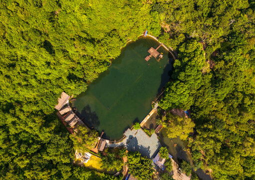 Aerial view of the lush green landscape surrounding a tranquil pond on Cat Ba Island with small wooden structures and a platform in Cat Hai, Hai Phong, Vietnam.