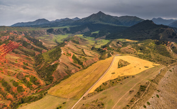 Aerial view of Seven Bulls Rock with dramatic red sandstone cliffs, rolling green hills, and golden wheat fields in Dzhetyoguz, Issyk-Kul Region, Kyrgyzstan.