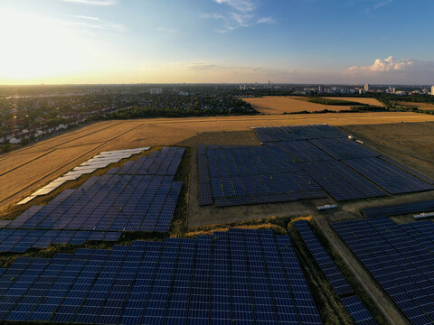 Aerial view of a solar farm with rows of photovoltaic panels set against golden fields and the distant Berlin skyline with its iconic TV tower in Schonefeld, Brandenburg, Germany.
