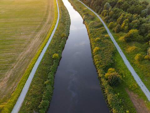Aerial view of the La Senne river flowing through rural agricultural fields and lush greenery during sunset in Zemst, Flanders, Belgium.