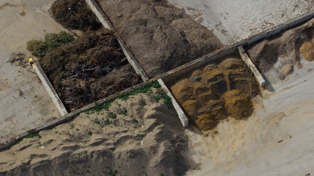 Aerial view of piles of organic waste, soil, and debris separated by concrete walls at an industrial site in La Longueville, Hauts-de-France, France.