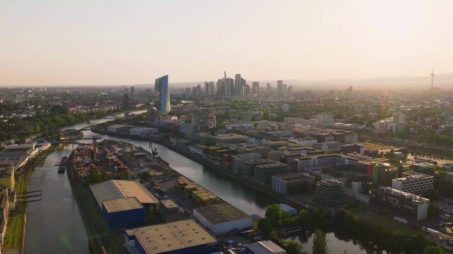 Aerial view of Osthafen, the industrial harbor area with warehouses and the Main river flowing towards the city skyline in Frankfurt am Main, Hessen, Germany.