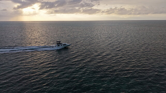 Aerial view of a motorboat cruising across the calm sea during a golden sunset in Belize, Belize.