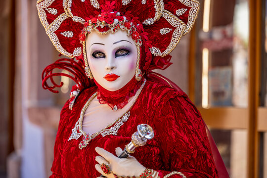 Riquewihr, Grand Est, France - 04 July 2026: View of a person wearing an elaborate red velvet costume and a decorative Venetian mask with intricate gold details and a matching headpiece.