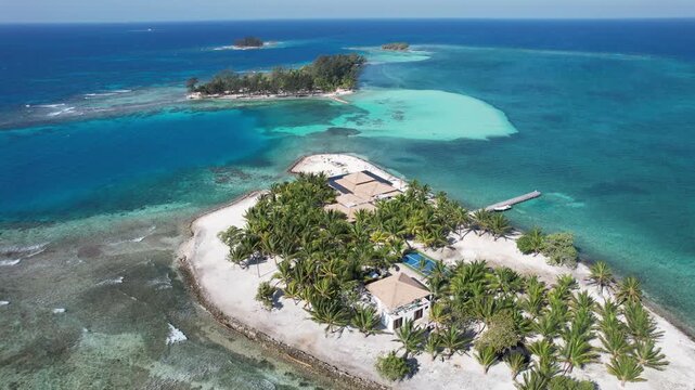 Aerial view of the tropical island of Utila with lush palm trees, private buildings, and a helipad surrounded by clear turquoise coral reefs in Utila, Bay Islands Department, Honduras.
