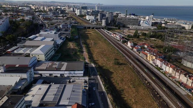 Aerial view of the urban landscape of Parque das Nacoes with railway tracks, modern buildings, and the Tagus River in the background in Lisbon, Lisbon, Portugal.
