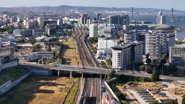 Aerial view of the modern Parque das Nacoes district with railway tracks, urban buildings, and the Vasco da Gama bridge in the background in Lisbon, Lisbon, Portugal.