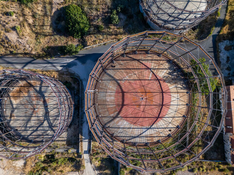 Aerial view of the historic gasometer silos featuring circular metal frameworks and red circular bases surrounded by roads and terrain in Lisboa, Lisboa, Portugal.