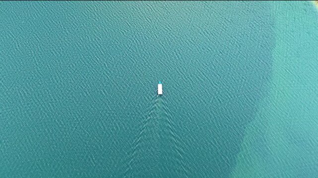 Aerial view of a small boat moving across the turquoise waters of Wadaslintang Reservoir in Wadaslintang, Central Java, Indonesia.