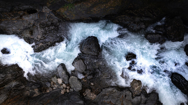 Aerial view of a rushing mountain stream flowing over dark jagged rocks in the wilderness of Puerto Williams, Magallanes, Chile.