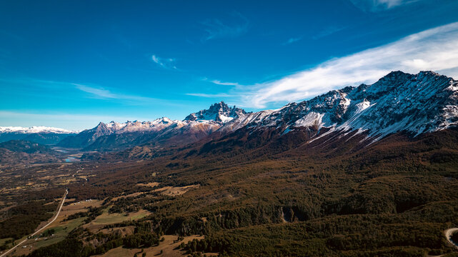 Aerial view of snow-capped peaks in Chilean Patagonia, with forests and winding roads under a clear blue sky in Cerro Castillo, Chile