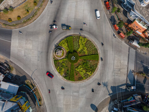 Aerial view of a roundabout with a landscaped central garden and small monument, surrounded by concrete roads with light traffic in Banyumas Regency, Central Java, Indonesia.