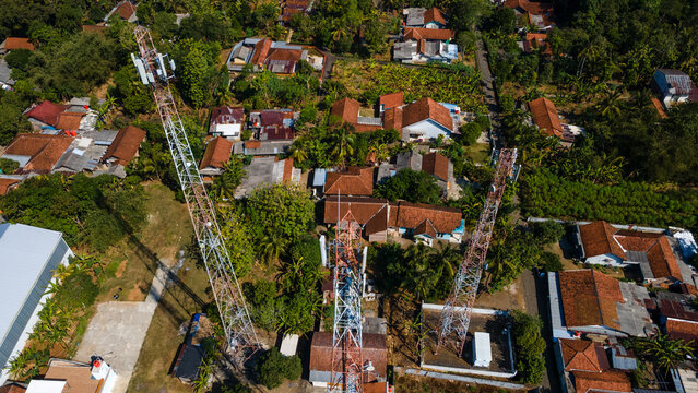 Aerial view of telecommunication towers standing among residential houses and lush tropical trees in Sumpiuh, Banyumas, Central Java, Indonesia.