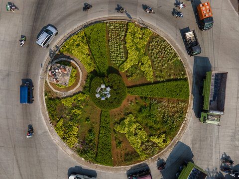 Aerial view of a roundabout featuring geometric garden landscaping, a small monument, and traffic including cars, trucks, and motorcycles in Banyumas Regency, Central Java, Indonesia.