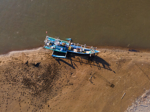 Aerial view of a traditional blue wooden fishing boat resting on the sandy shore with visible footprints in the sand in Kebumen, Central Java, Indonesia.