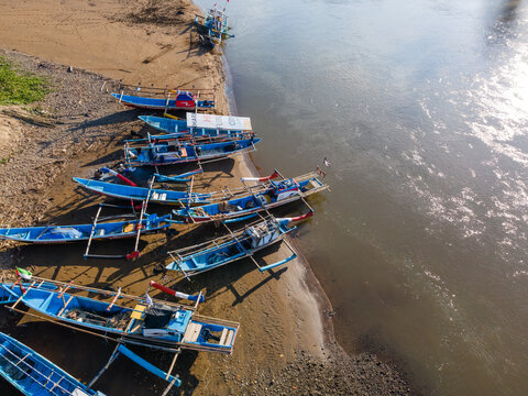 Aerial view of traditional wooden fishing boats moored along the sandy riverbank in Kebumen, Central Java, Indonesia.