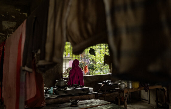 Banshkhali Upazila, Chittagong Division, Bangladesh - 12 July 2026: View of a woman in a pink hijab looking out a window in a dim kitchen with laundry hanging in the foreground.