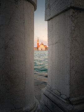 View of San Giorgio Maggiore church across the water framed by ancient stone columns at sunset in Venezia, Veneto, Italy.