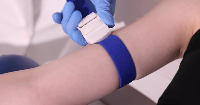 Doctor applying medical tourniquet on patient's arm indoors, closeup
