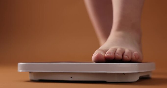 Overweight woman stepping on scale against brown background, closeup