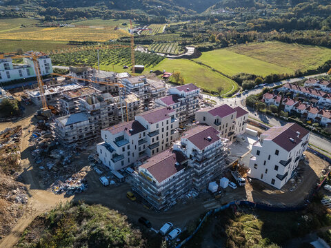 Aerial view of the construction site at Juzna cesta featuring new residential buildings with scaffolding and cranes surrounded by green fields in Izola, Izola, Slovenia.