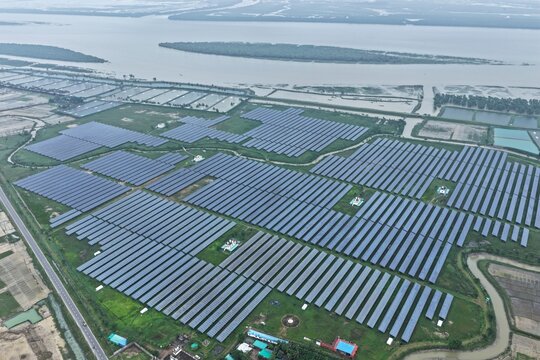Aerial view of a large solar farm with rows of photovoltaic panels installed on green land near a river in Ukhia, Chittagong Division, Bangladesh.